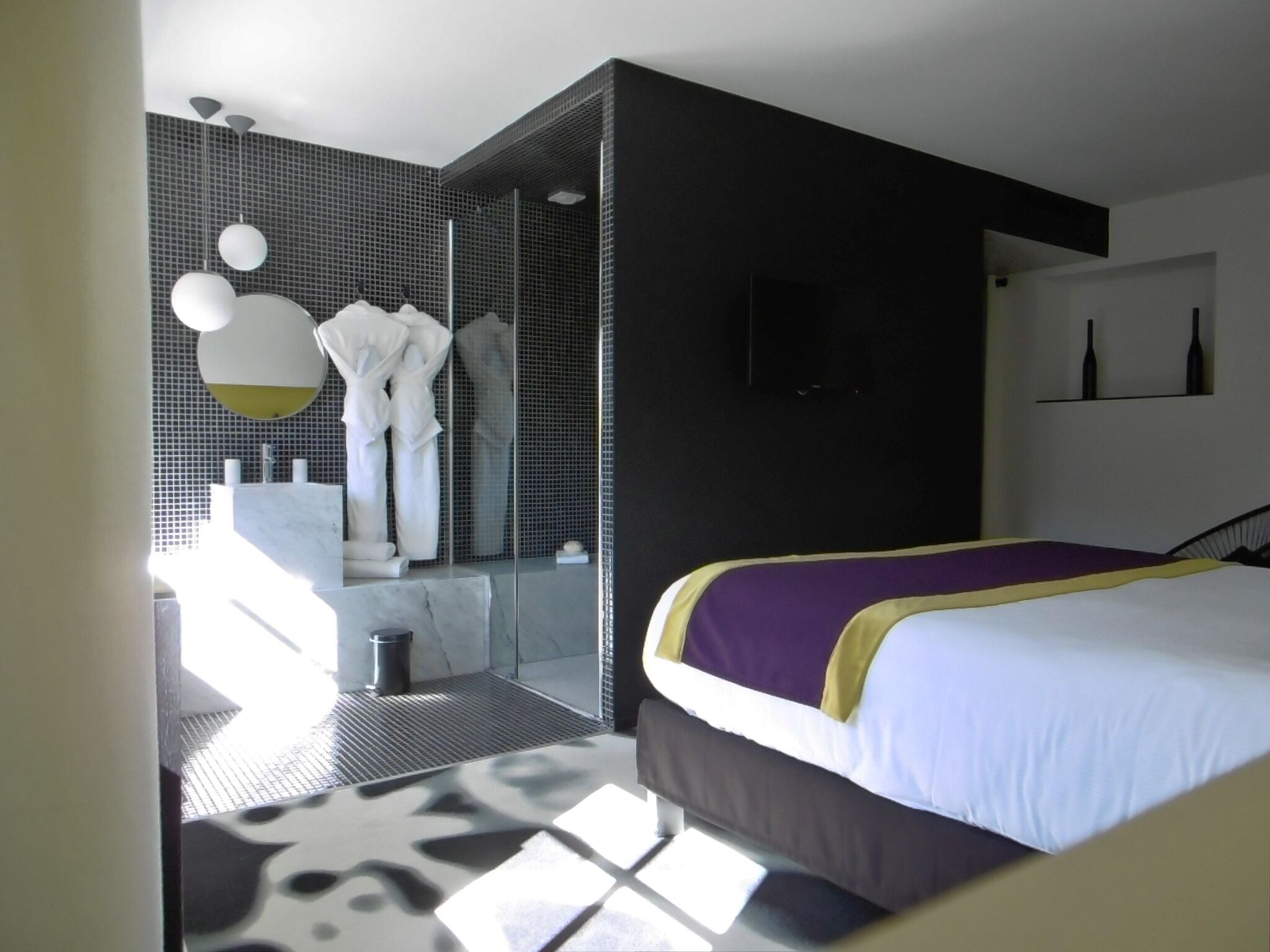 Ein modernes Hotelzimmer mit einem großen Bett, einem separaten Badezimmer mit Dusche und einem an der Wand befestigten Flachbildfernseher.