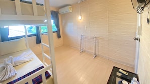 A room with bunk beds, a small table with a remote control, and a window with curtains. - Steve Lady Hostel (Bangkok)