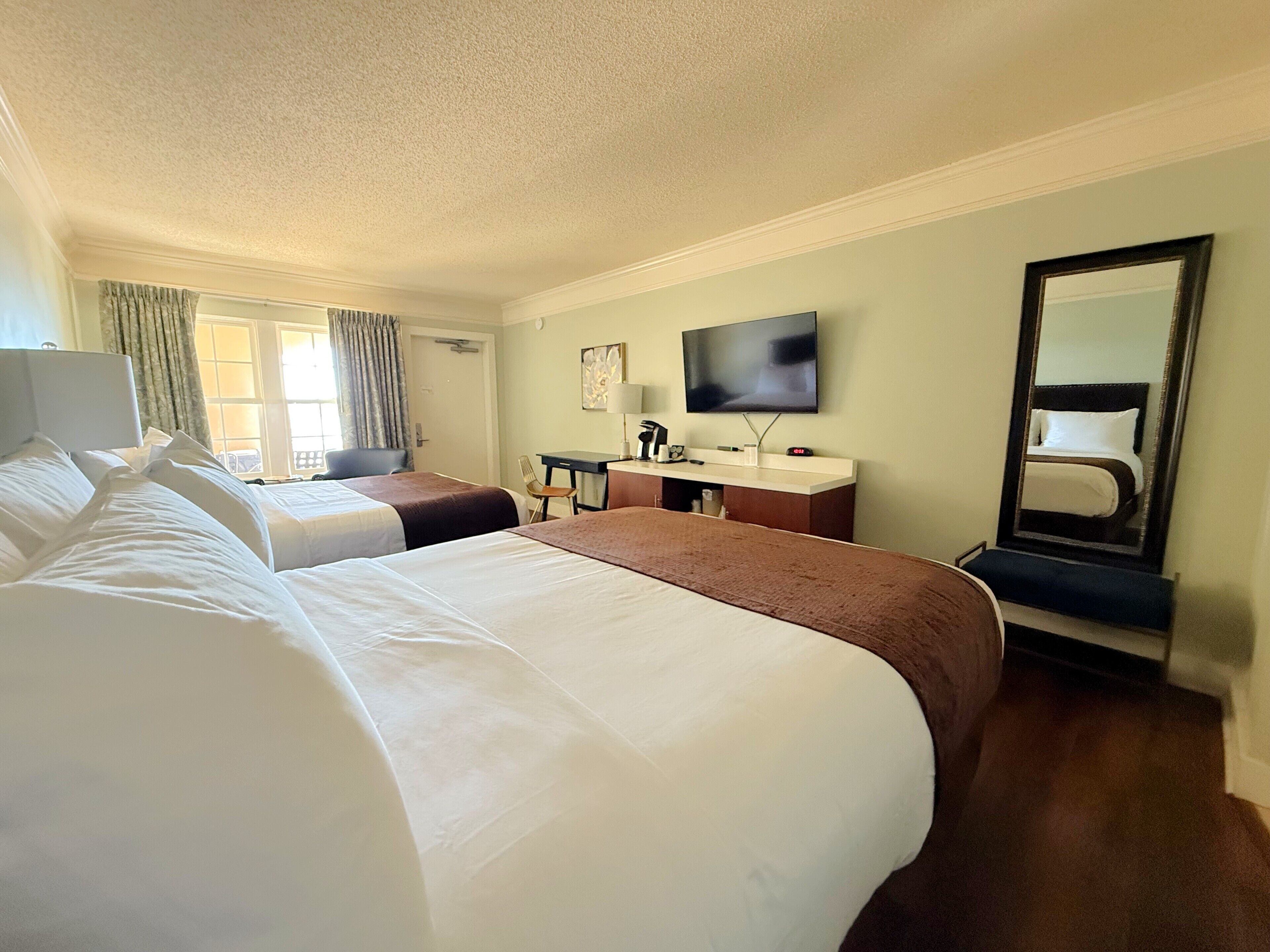 Een hotelkamer met twee bedden, een bureau, een televisie en een grote spiegel.