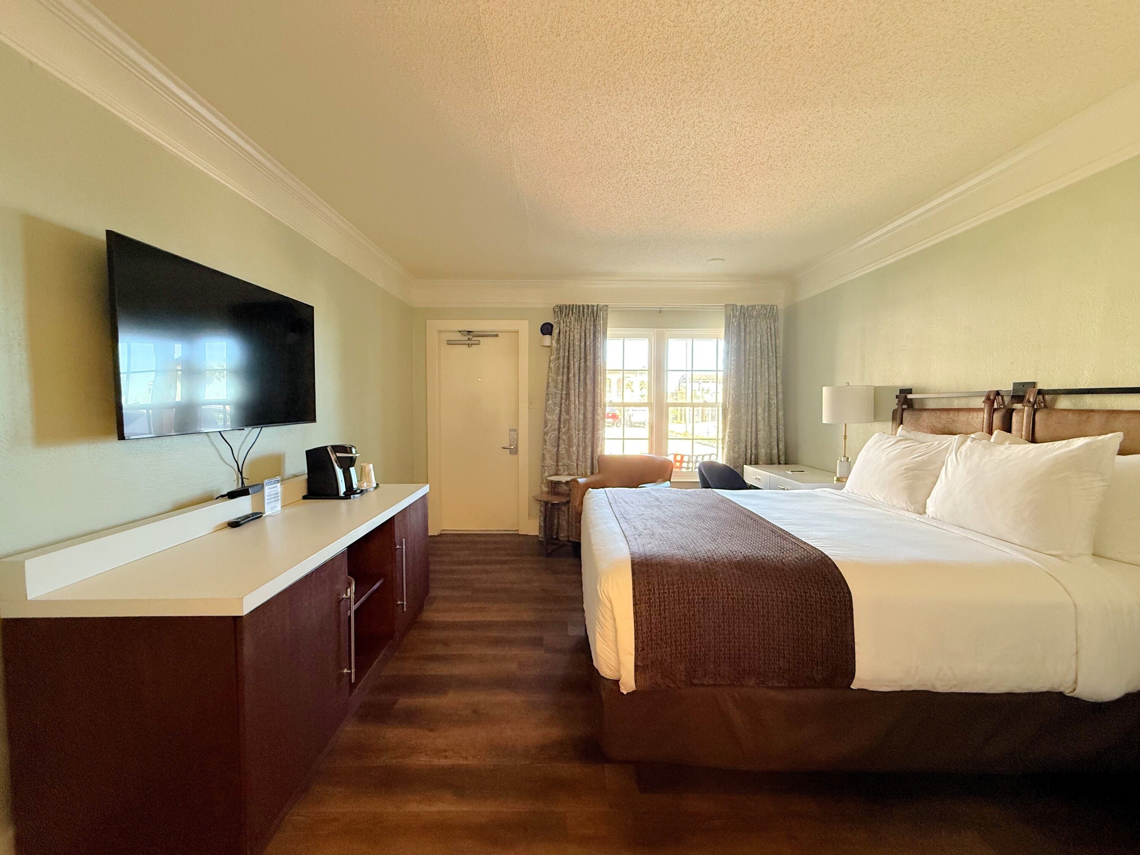 A hotel room with a bed, a desk, a television, and a window with curtains.