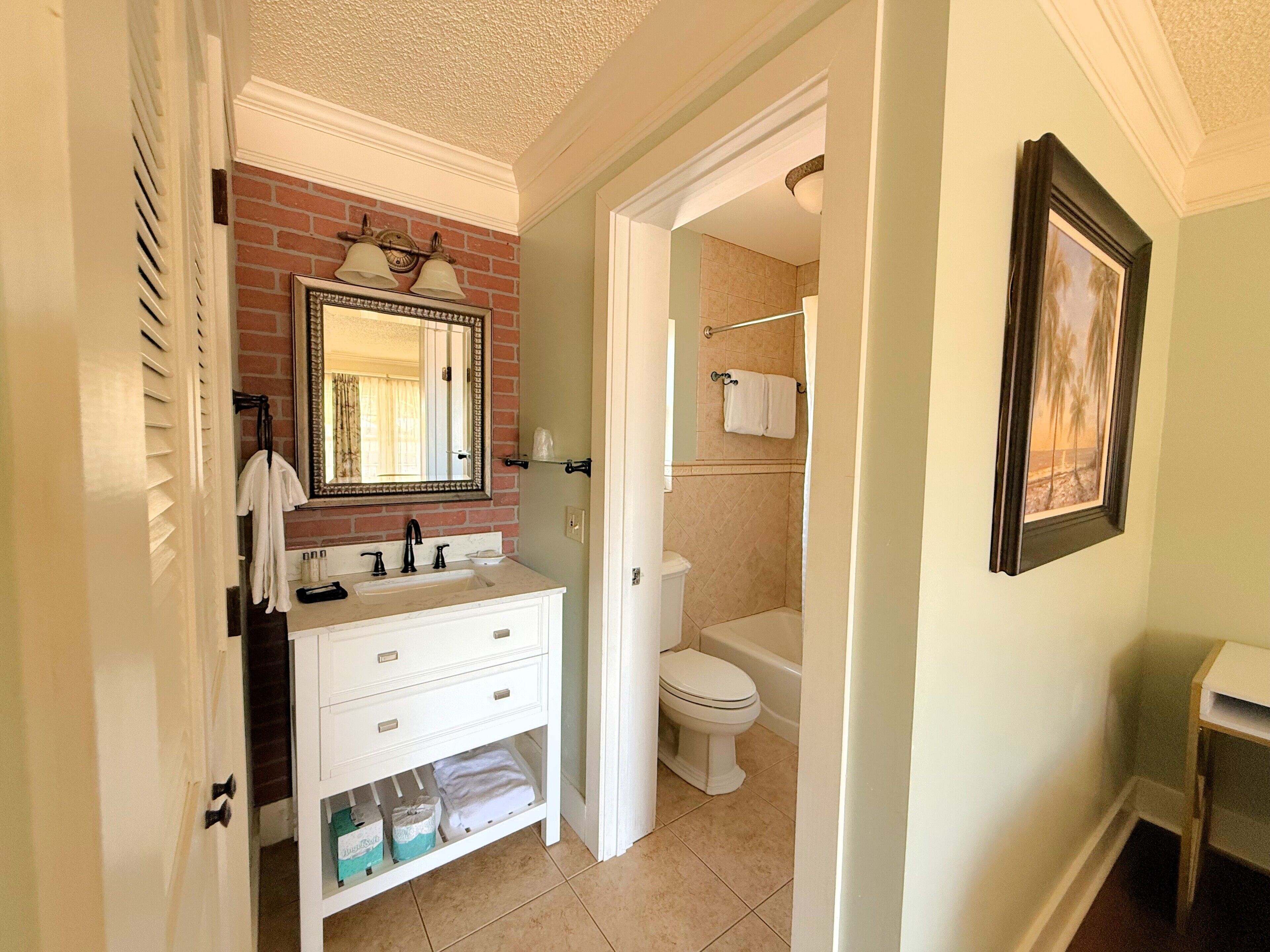 Un baño con tocador blanco, espejo con marco decorativo, inodoro y zona de ducha.
