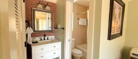 Une salle de bain avec un meuble-lavabo blanc, un miroir doté d’un cadre décoratif, des toilettes et un espace douche.