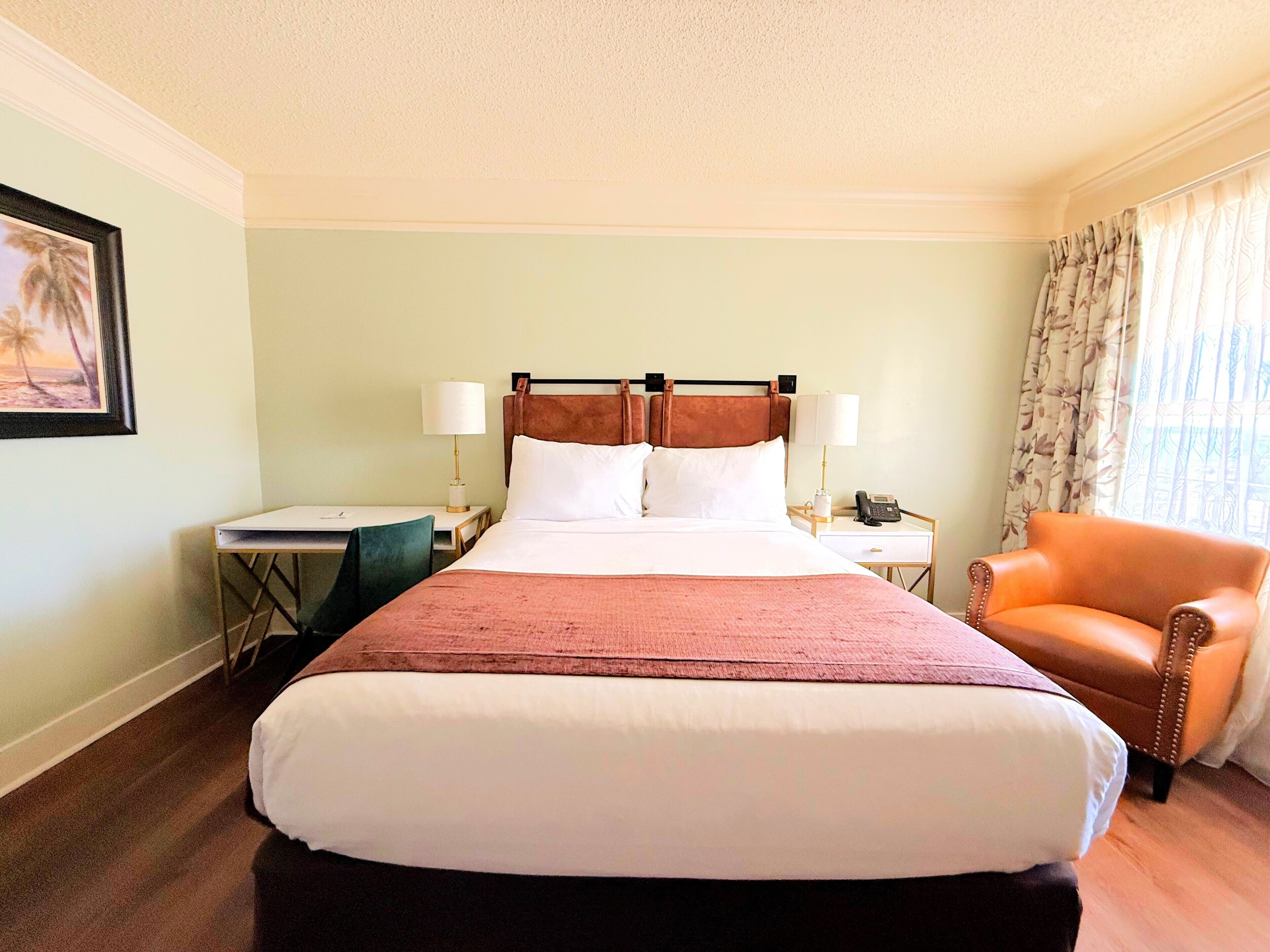 A hotel room with a large bed, two bedside tables with lamps, a chair, and a framed picture on the wall.