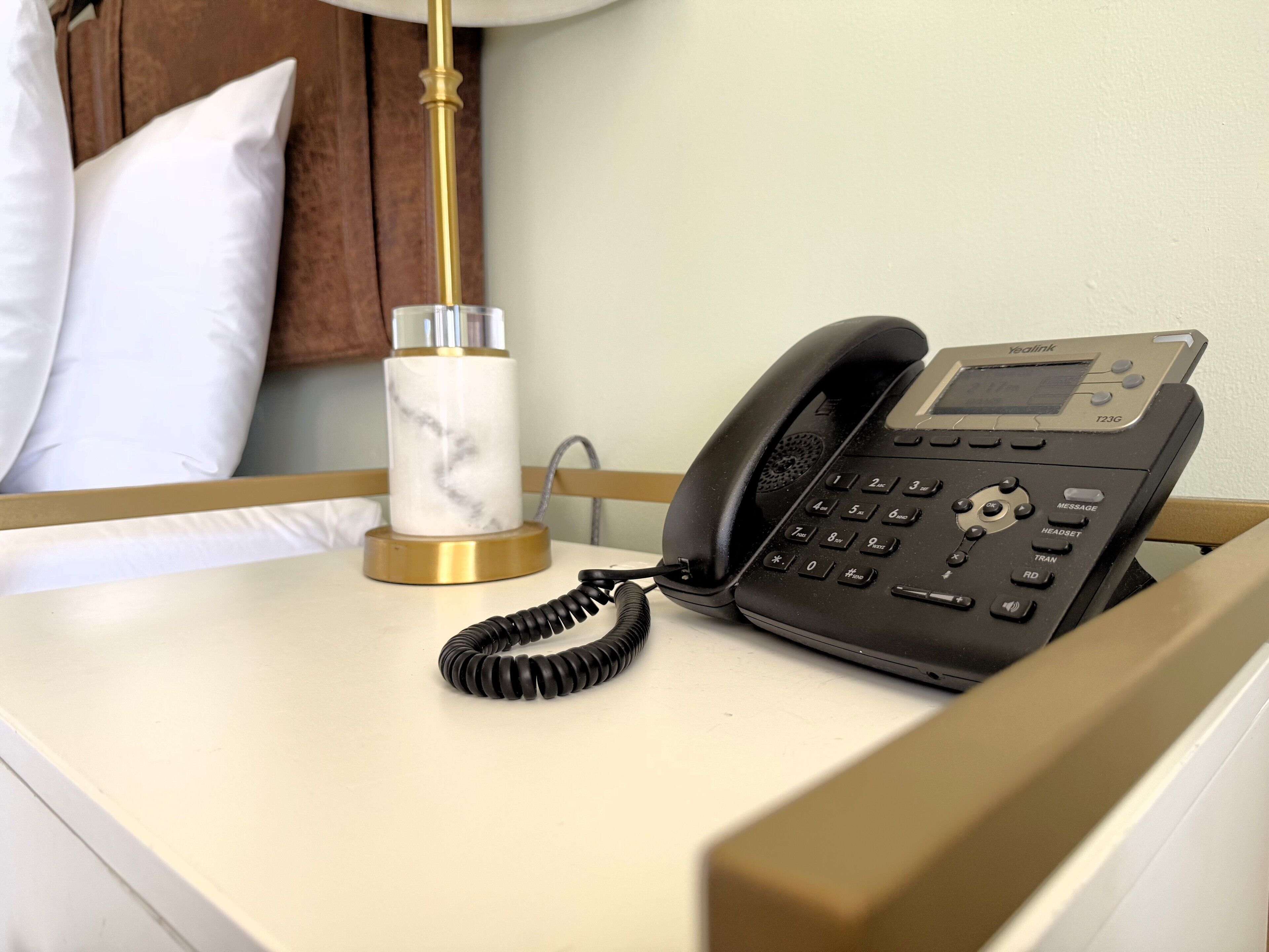 Una habitación de hotel con una mesita de noche, un teléfono negro y un candelabro de mármol.