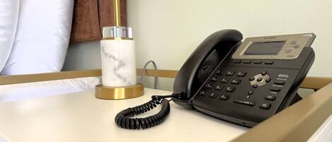 Una habitación de hotel con una mesita de noche, un teléfono negro y un candelabro de mármol.