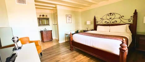A hotel room with a wooden bed, a desk with a telephone, a chair, a dresser, and a mirror on the wall.