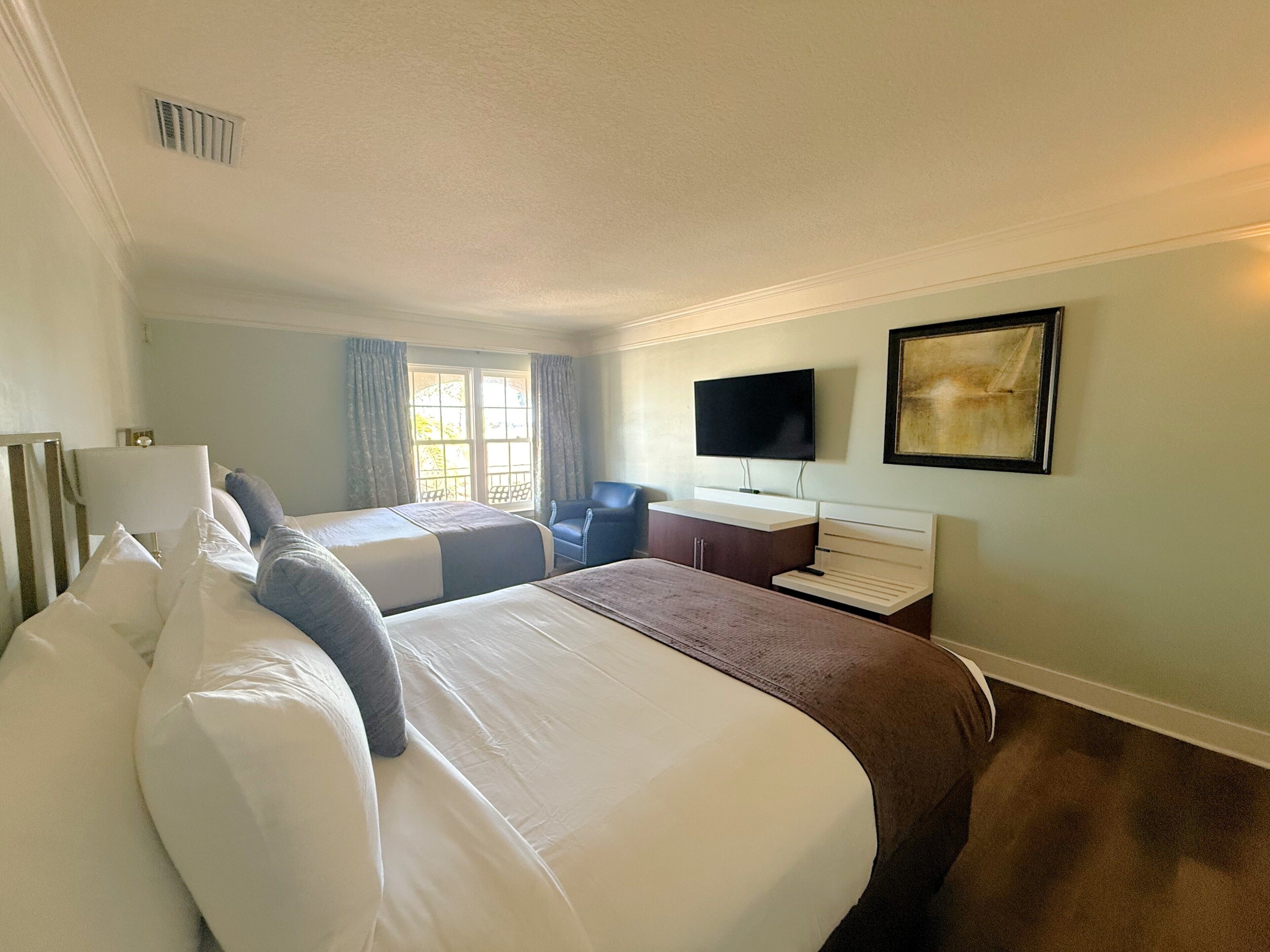 A hotel room with two beds, a desk, a chair, a television, and a window with curtains.