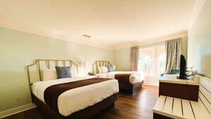 A hotel room with two beds, a desk, and a window with curtains.