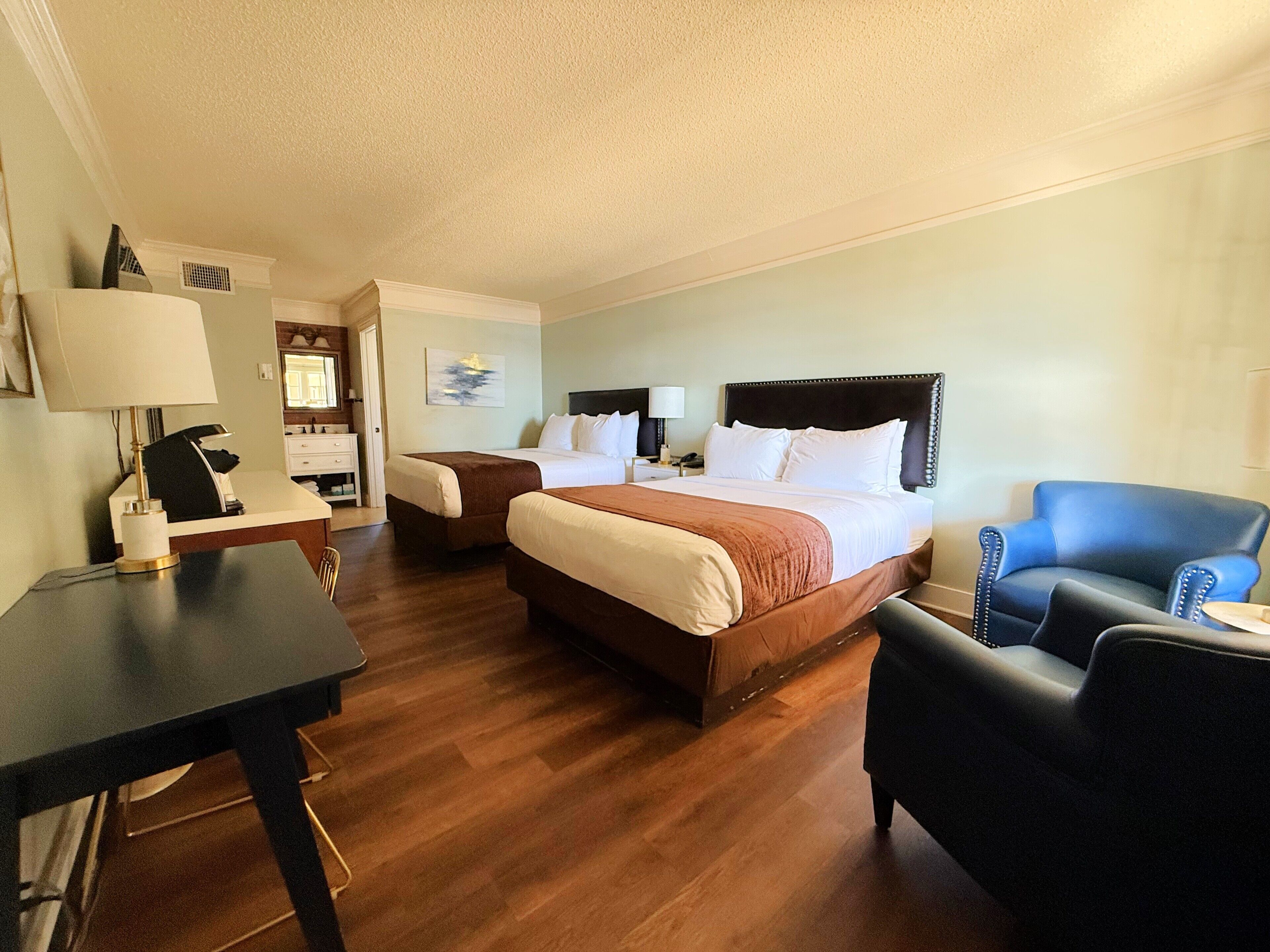 A hotel room with a large bed, a desk, a chair, and a small table.