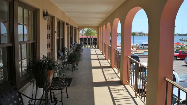 A covered balcony with a view of the water, potted plants, and outdoor seating.