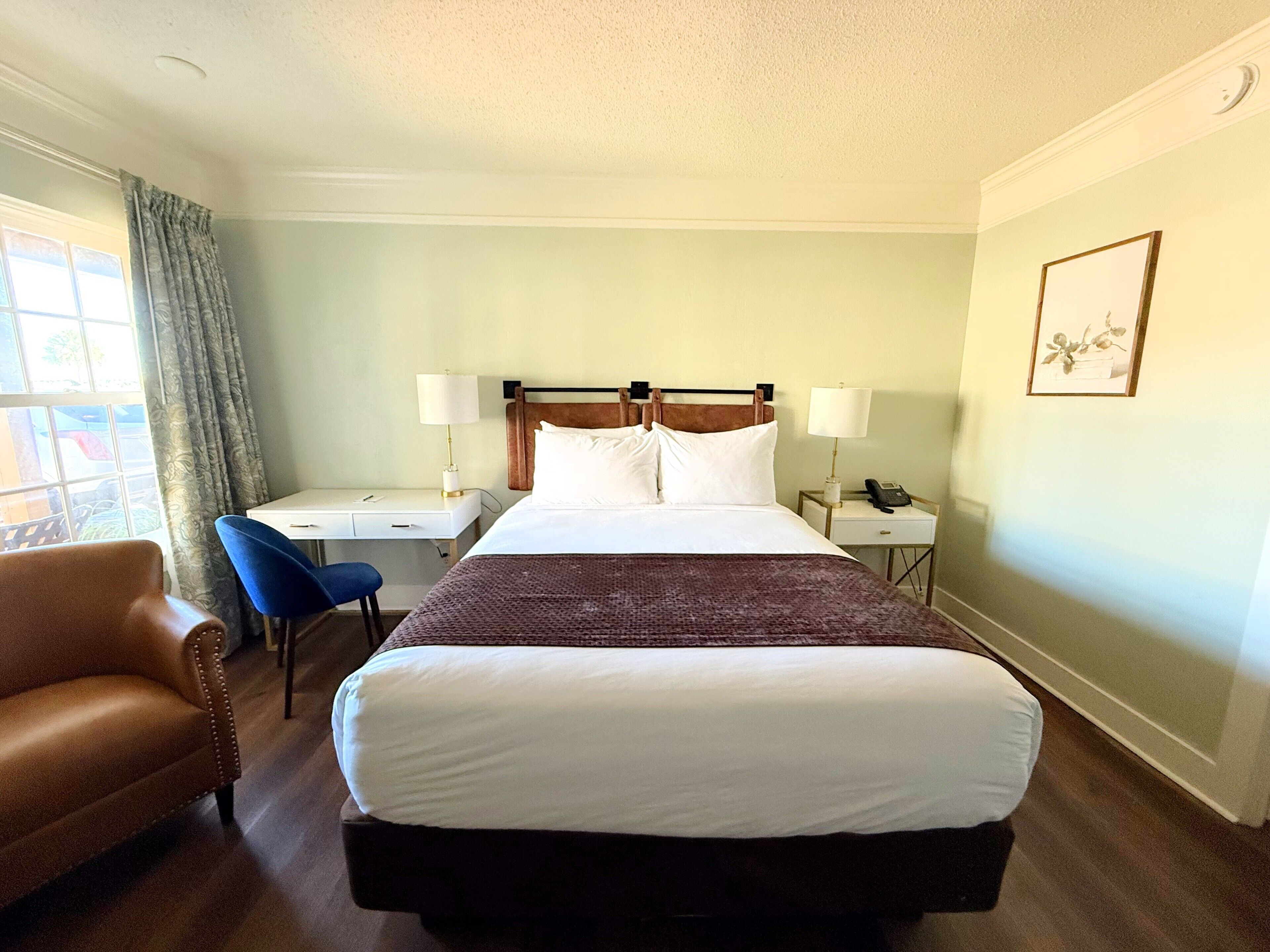 A hotel room with a large bed, a desk, a chair, a phone, and a window with curtains.