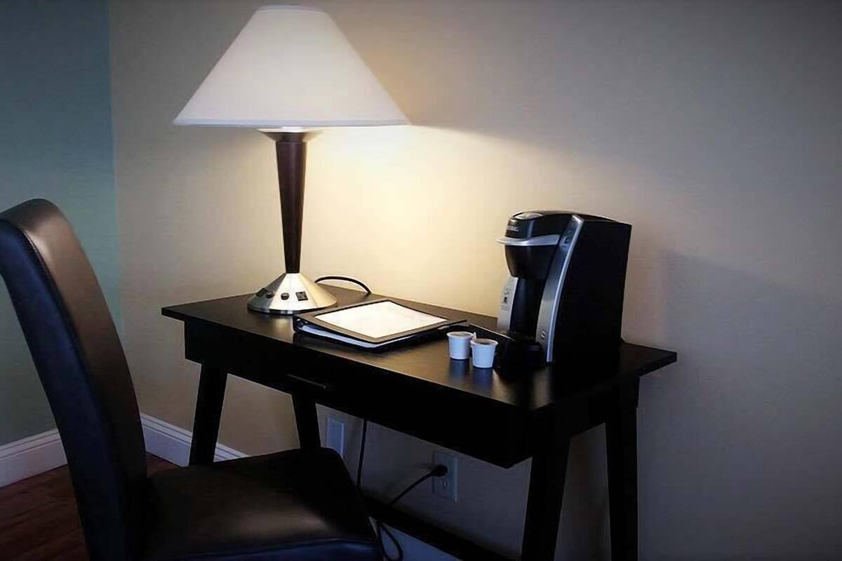A small desk with a lamp, a coffee maker, and a tablet.