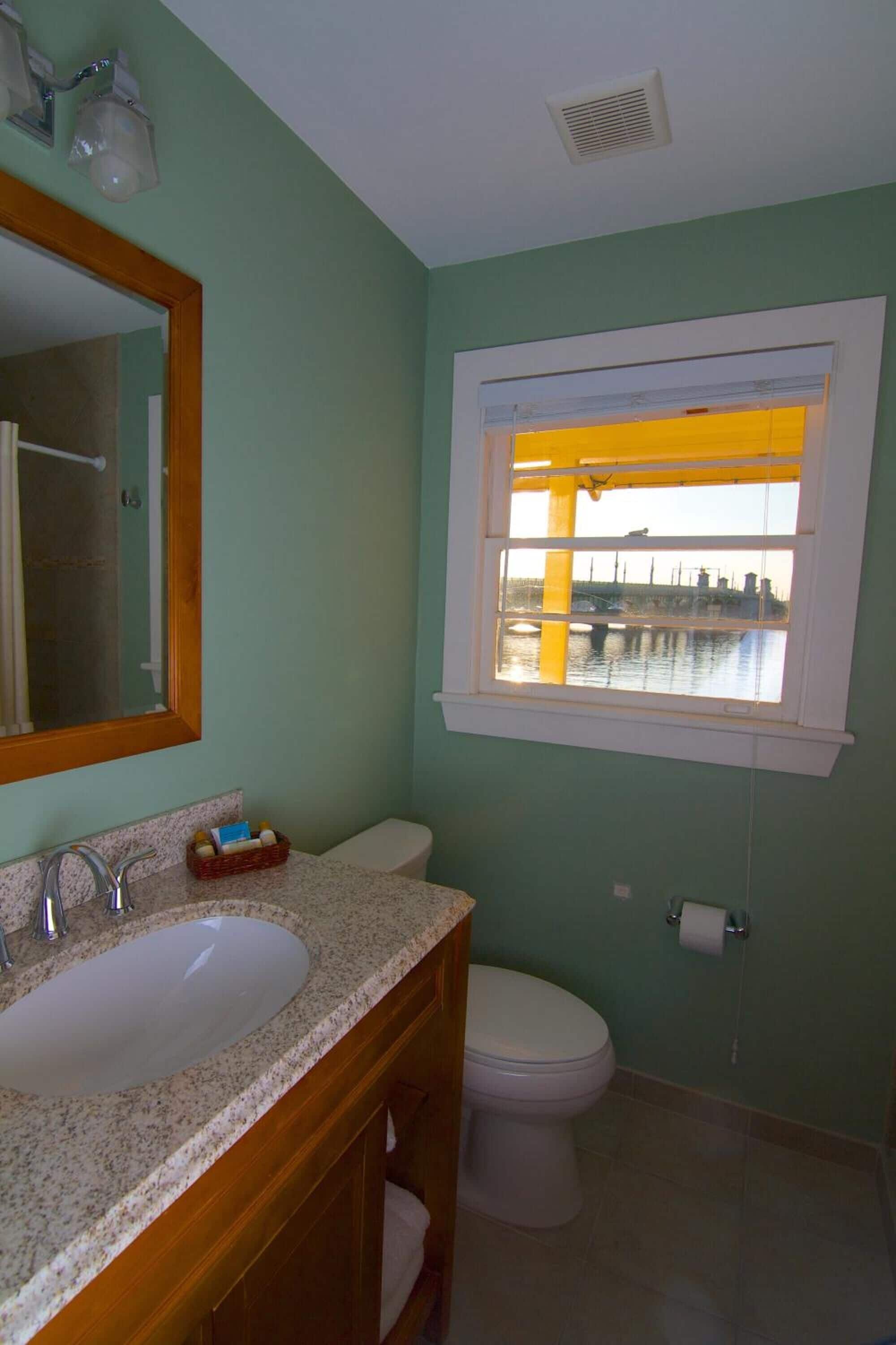 Une salle de bain équipée d’un lavabo, de toilettes et d’une fenêtre donnant sur un pont et sur l’eau.