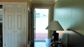 A hotel room with a bed, a nightstand, a lamp, and a door leading to a hallway.