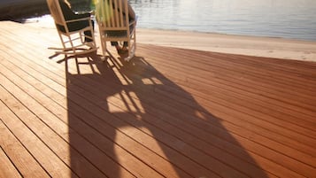 Une terrasse en bois avec deux fauteuils à bascule donnant sur un plan d’eau paisible.