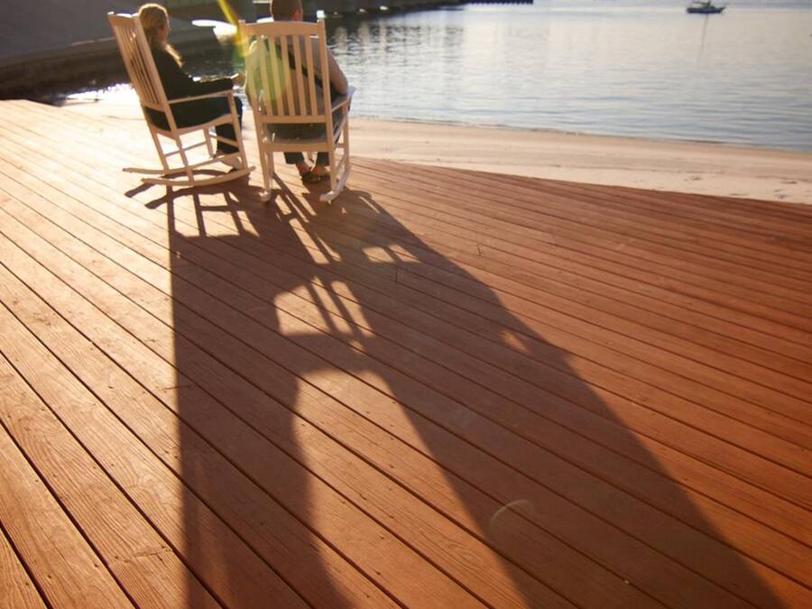 Une terrasse en bois avec deux fauteuils à bascule donnant sur un plan d’eau paisible.