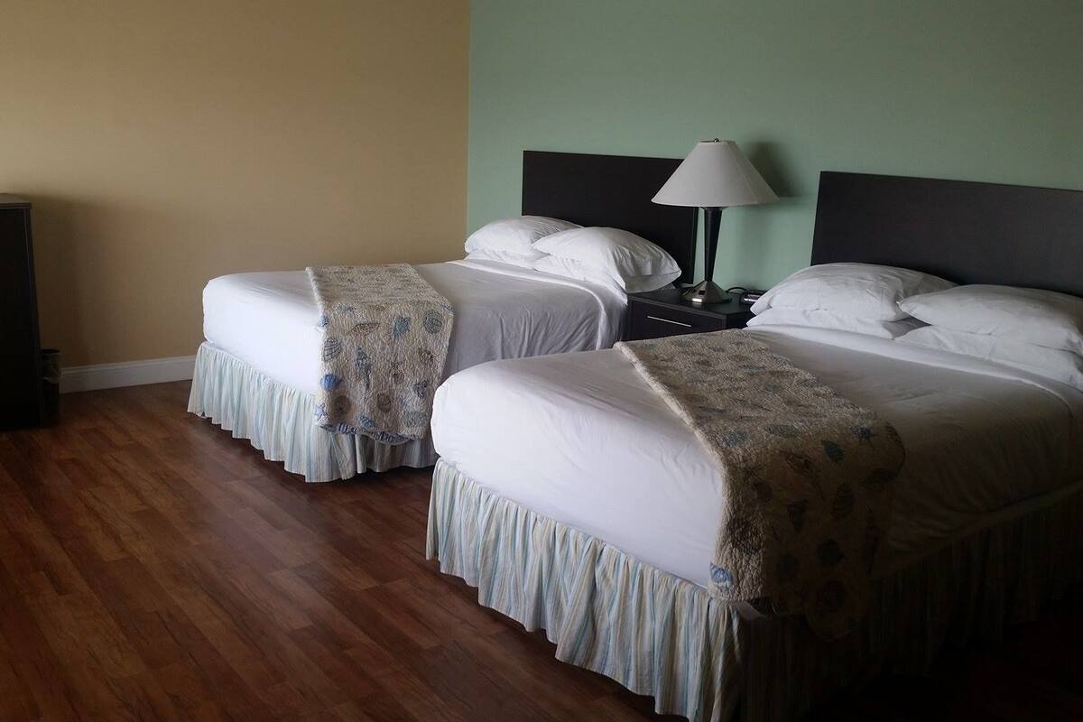 A hotel room with two beds, a nightstand, a lamp, and a wooden floor.