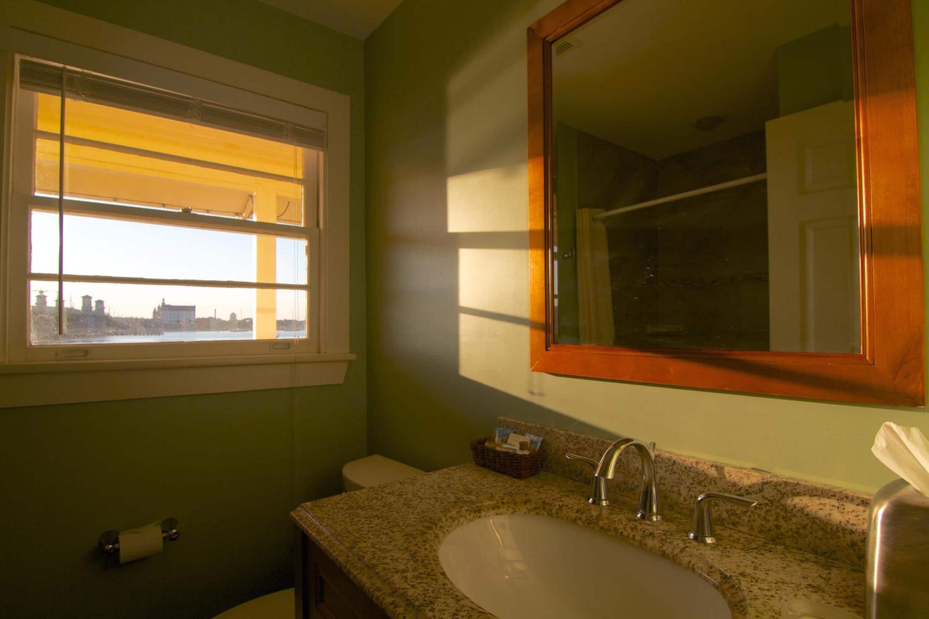 A bathroom with a large window, a sink, and a mirror.