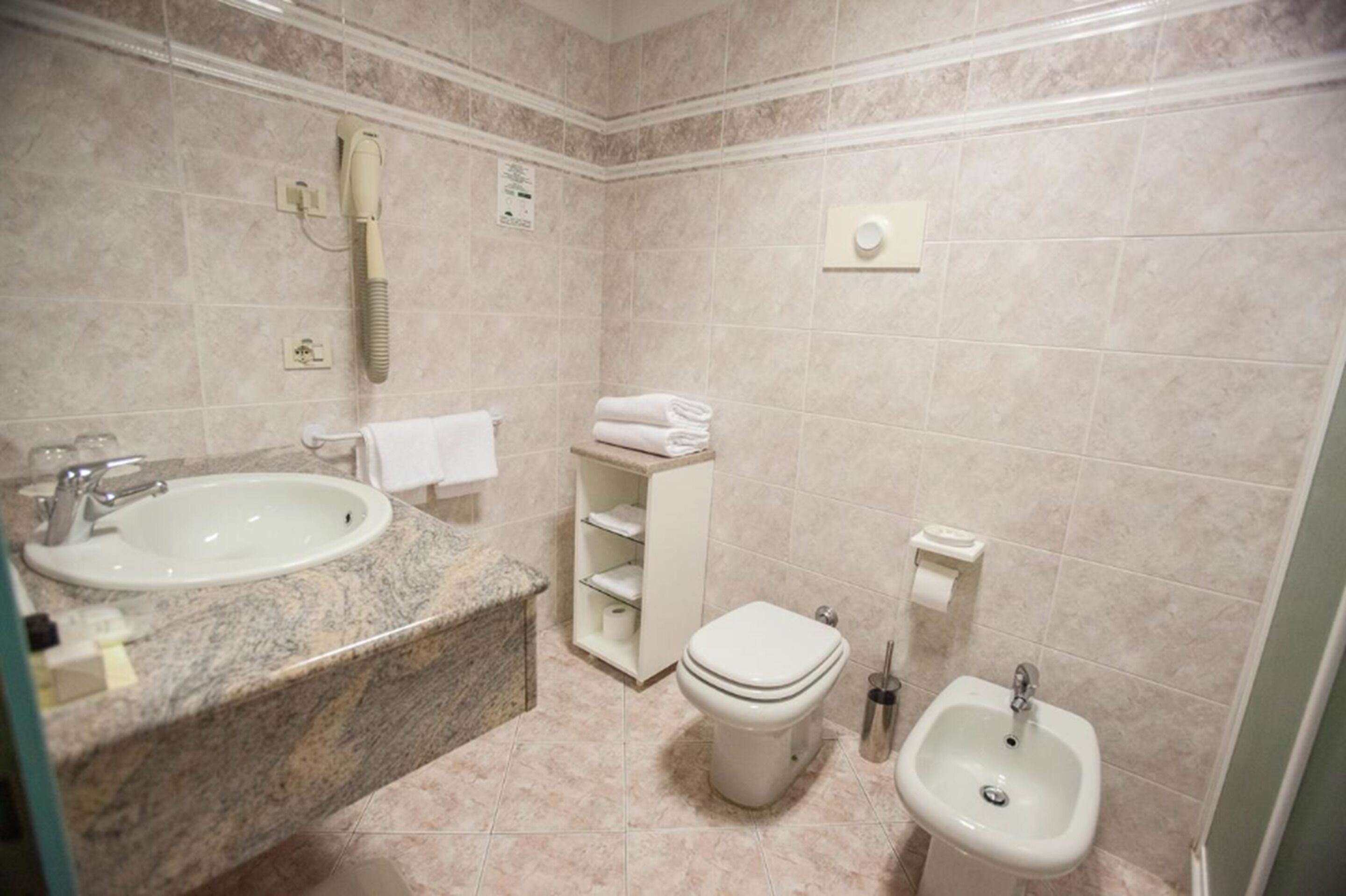 A bathroom with a sink, toilet, bidet, and towel storage.