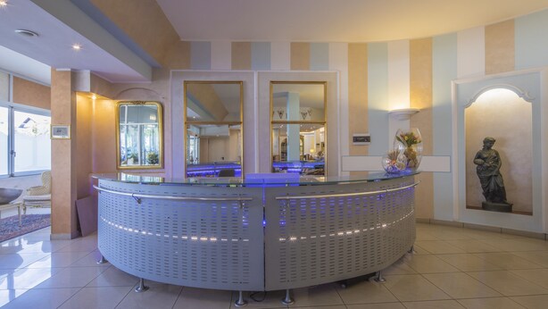 A reception area with a curved reception desk, two large mirrors, a statue, and a vase with flowers. - Hotel Ristorante Continental (Osio Sotto)