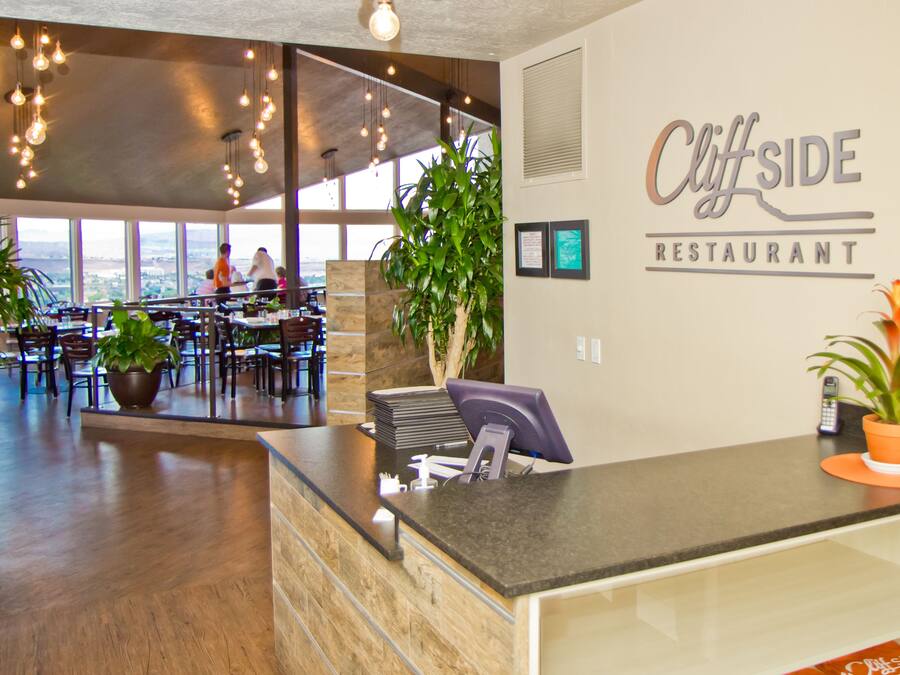 A restaurant interior with a reception desk, seating area, and large windows offering a view.