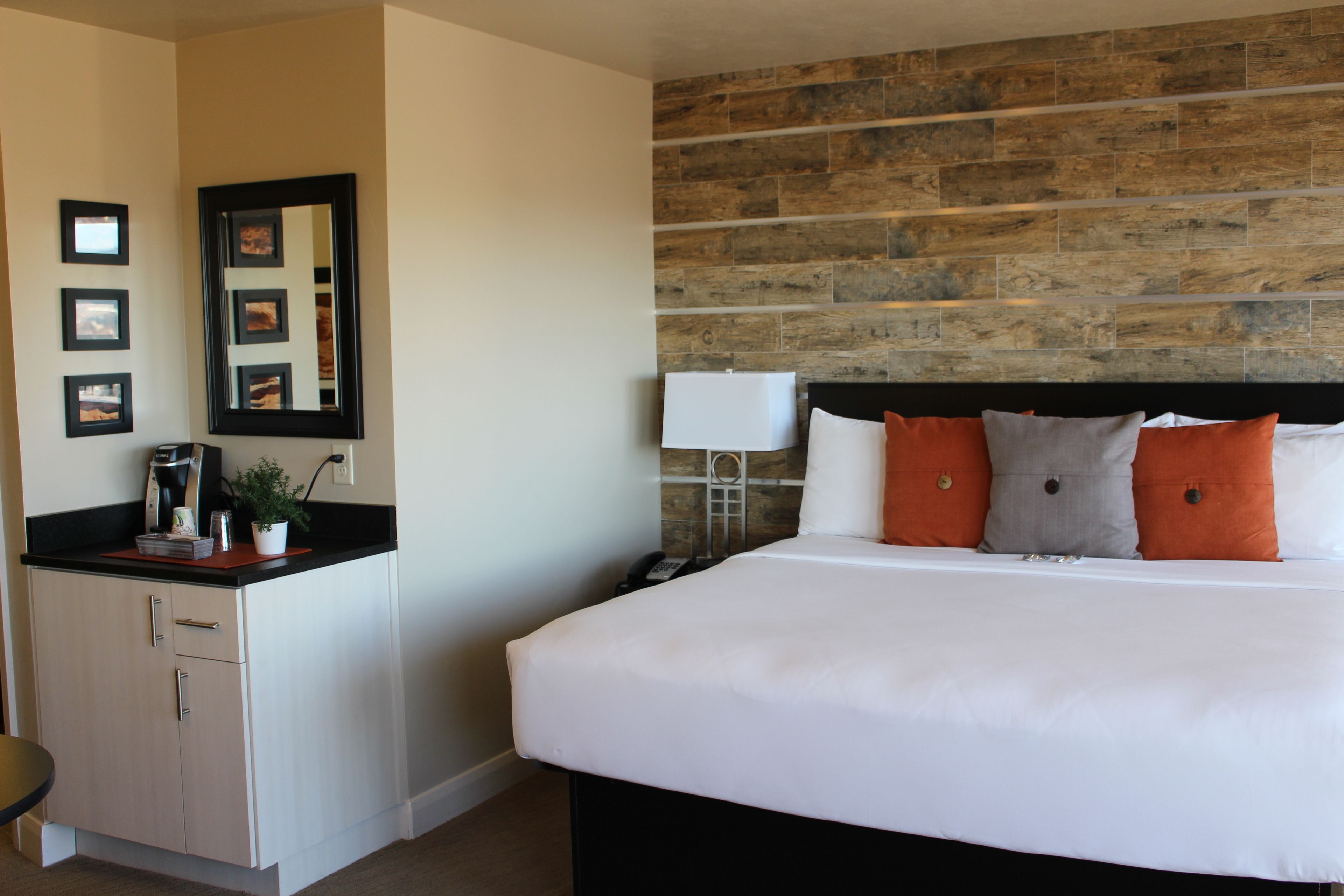 A hotel room with a large bed, a wooden accent wall, a desk with a lamp, and framed pictures on the wall.
