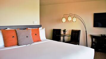 A hotel room with a large bed, a small table with chairs, a TV, and a unique wall-mounted lamp.