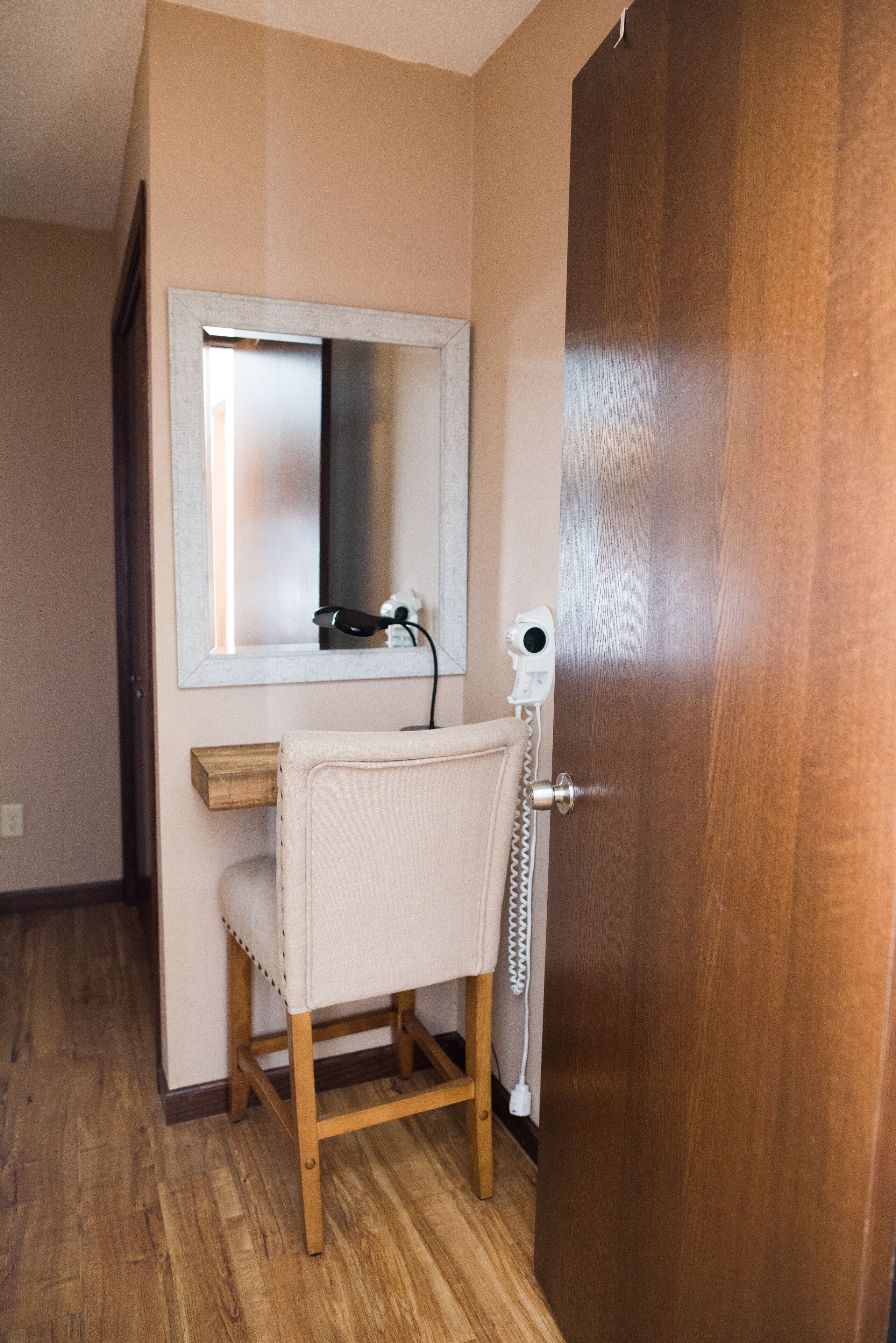 Een kleine badkamer met een houten stoel, een spiegel en een haardroger op een aanrecht.