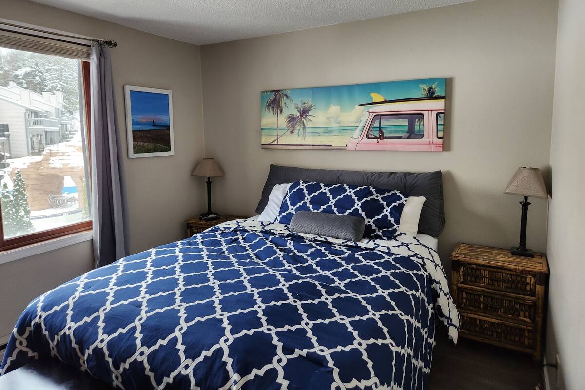 Ein Schlafzimmer mit einem Bett, einem Strandbild, einer Lampe und einer Holzkiste.