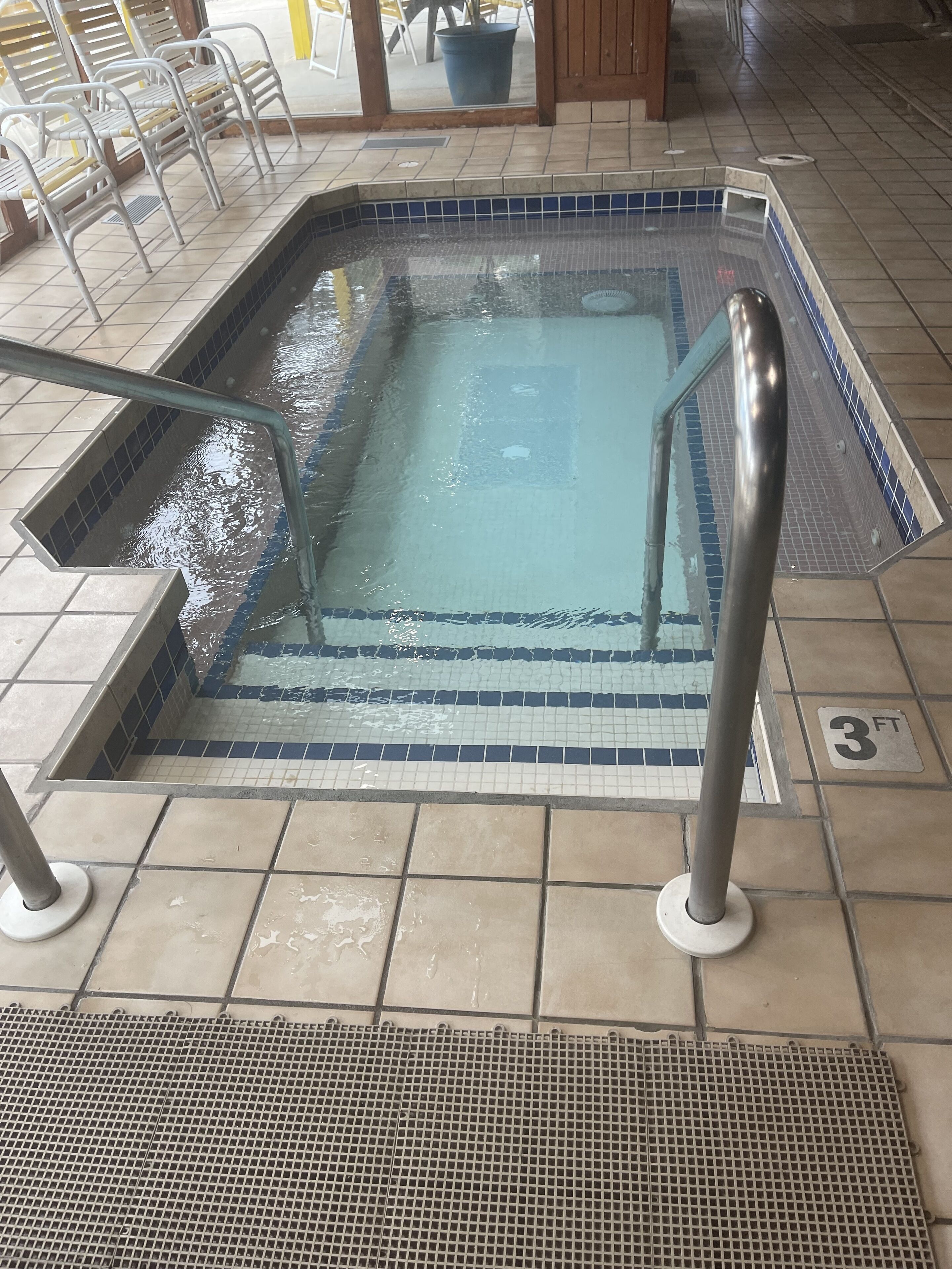 A swimming pool with tiled steps and metal railings.