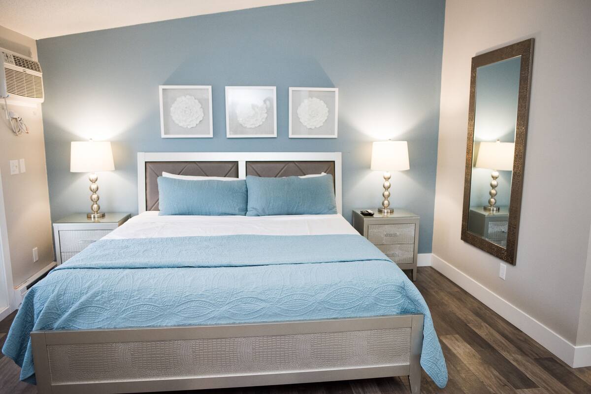 Ein Schlafzimmer mit einem Bett, zwei Nachttischen, einem Wandspiegel und drei gerahmten Bildern.