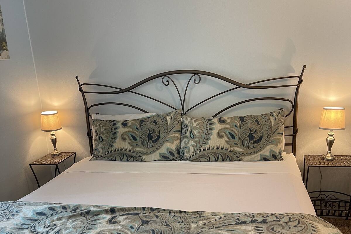 Ein Bett mit einem gemusterten Überwurf, zwei Nachttischlampen und einem Metall-Kopfteil.