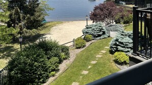 Uitzicht op een meer vanaf een balkon met een houten terras, een zandstrand en een boot afgemeerd op het water.