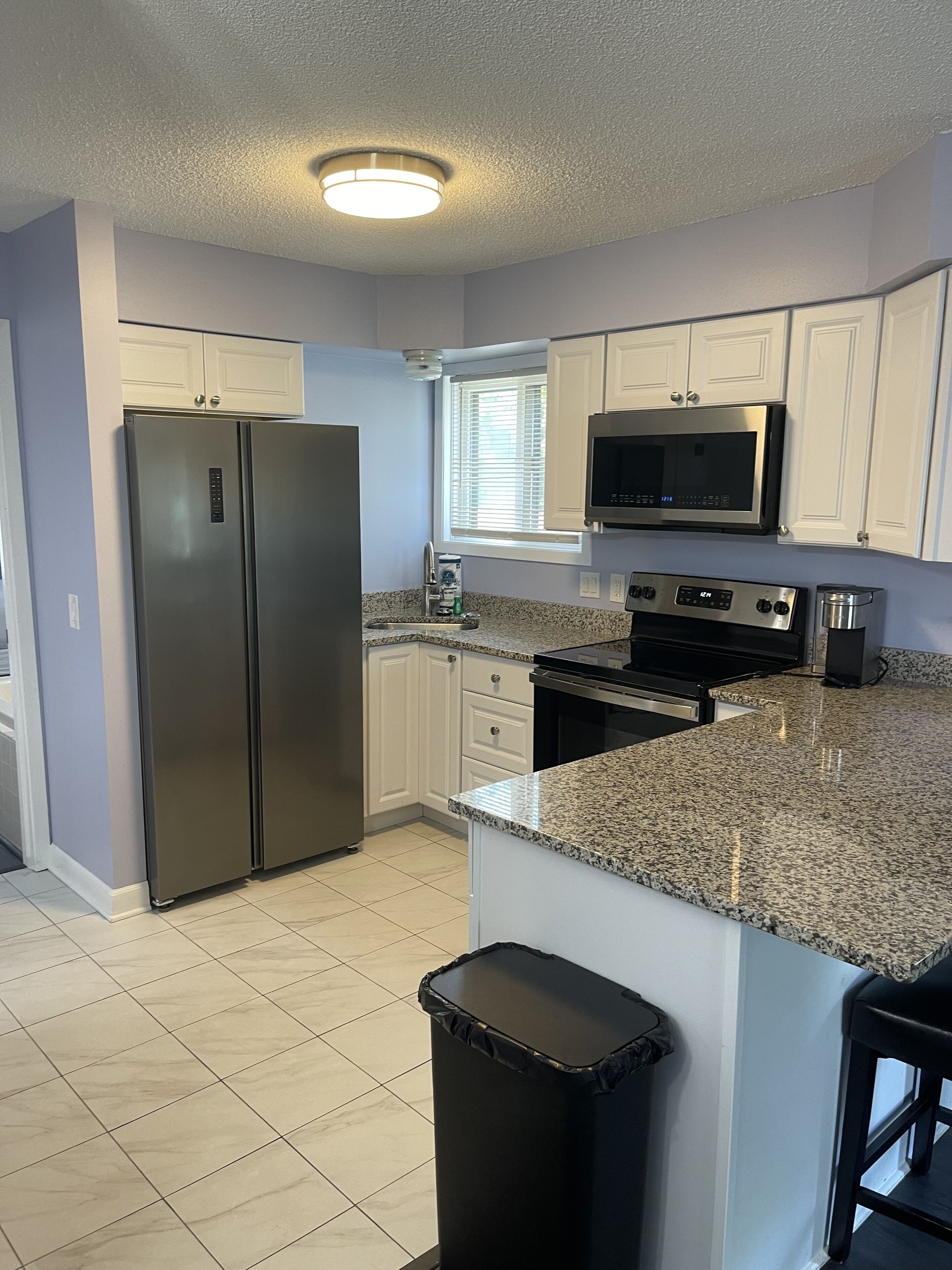 A modern kitchen with white cabinets, stainless steel appliances, a granite countertop, and a black trash bin.