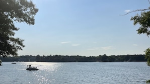 Een zandstrand met een kajak en stoelen, een boot op het water en een beboste kustlijn.