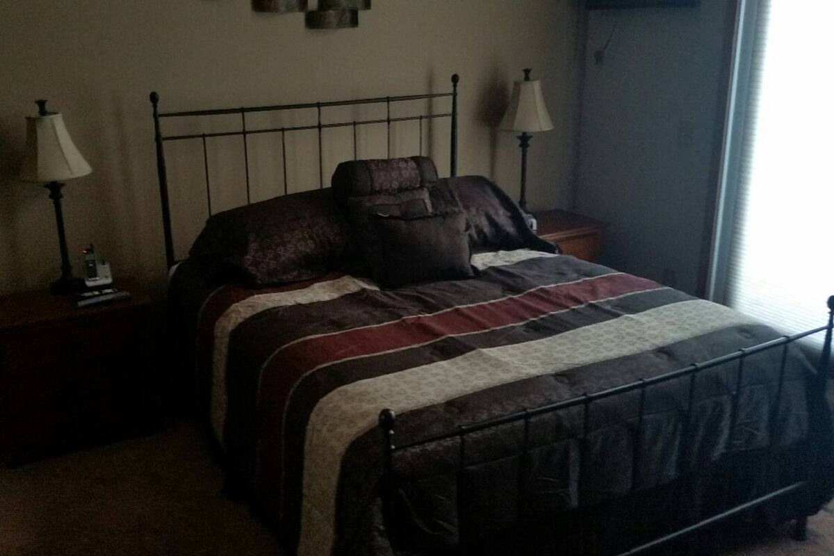 Ein Schlafzimmer mit einem Metallbettgestell, einer gestreiften Bettdecke, zwei Nachttischlampen und einem Nachttisch mit einer Lampe.