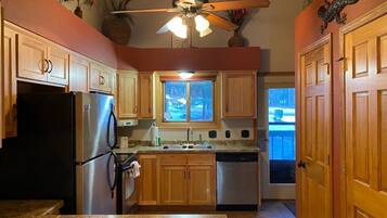 A kitchen with wooden cabinets, stainless steel appliances, a ceiling fan, and a window with a view of trees.