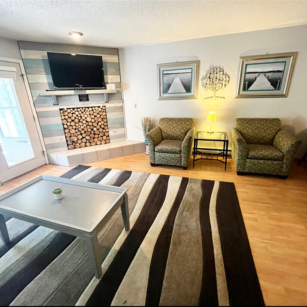 A living room with a TV, two armchairs, a coffee table, a rug, and a fireplace.
