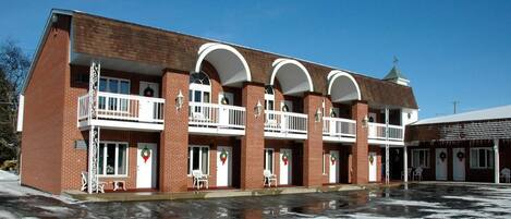 A multi-story brick building with balconies, each with a white railing and a wreath on the door.