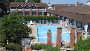 A pool area with lounge chairs, a brick building with arched windows, and a fenced pool.