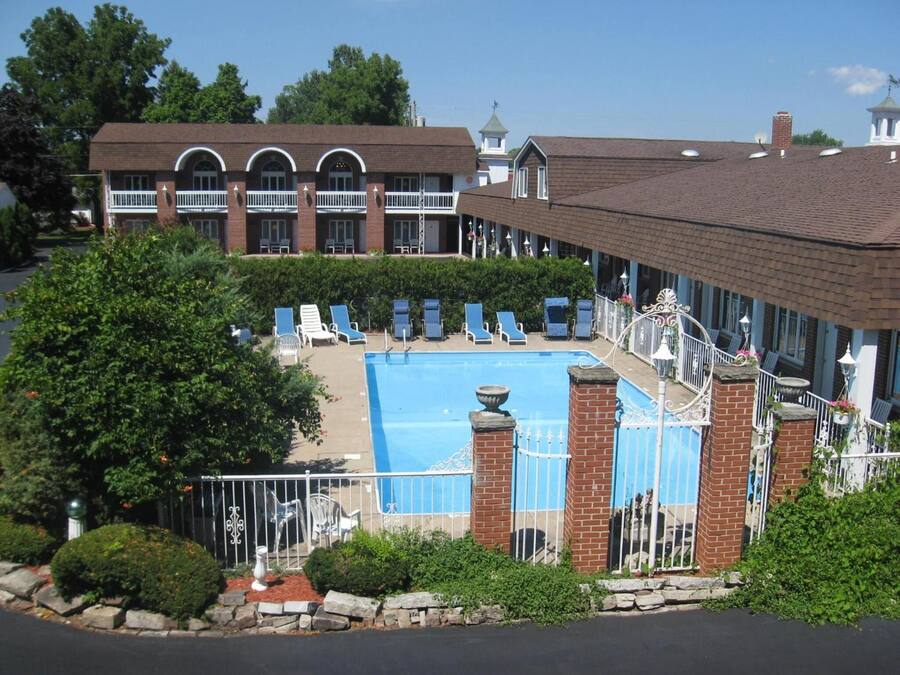 Área de piscina com espreguiçadeiras, um edifício de tijolo com janelas em arco e uma piscina cercada.
