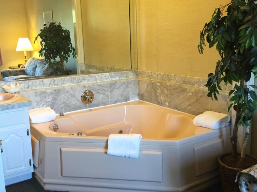 Eine große, freistehende Badewanne in einem Hotelbad mit Marmorwand, einem Spiegel, einem Waschbecken und einer Topfpflanze.