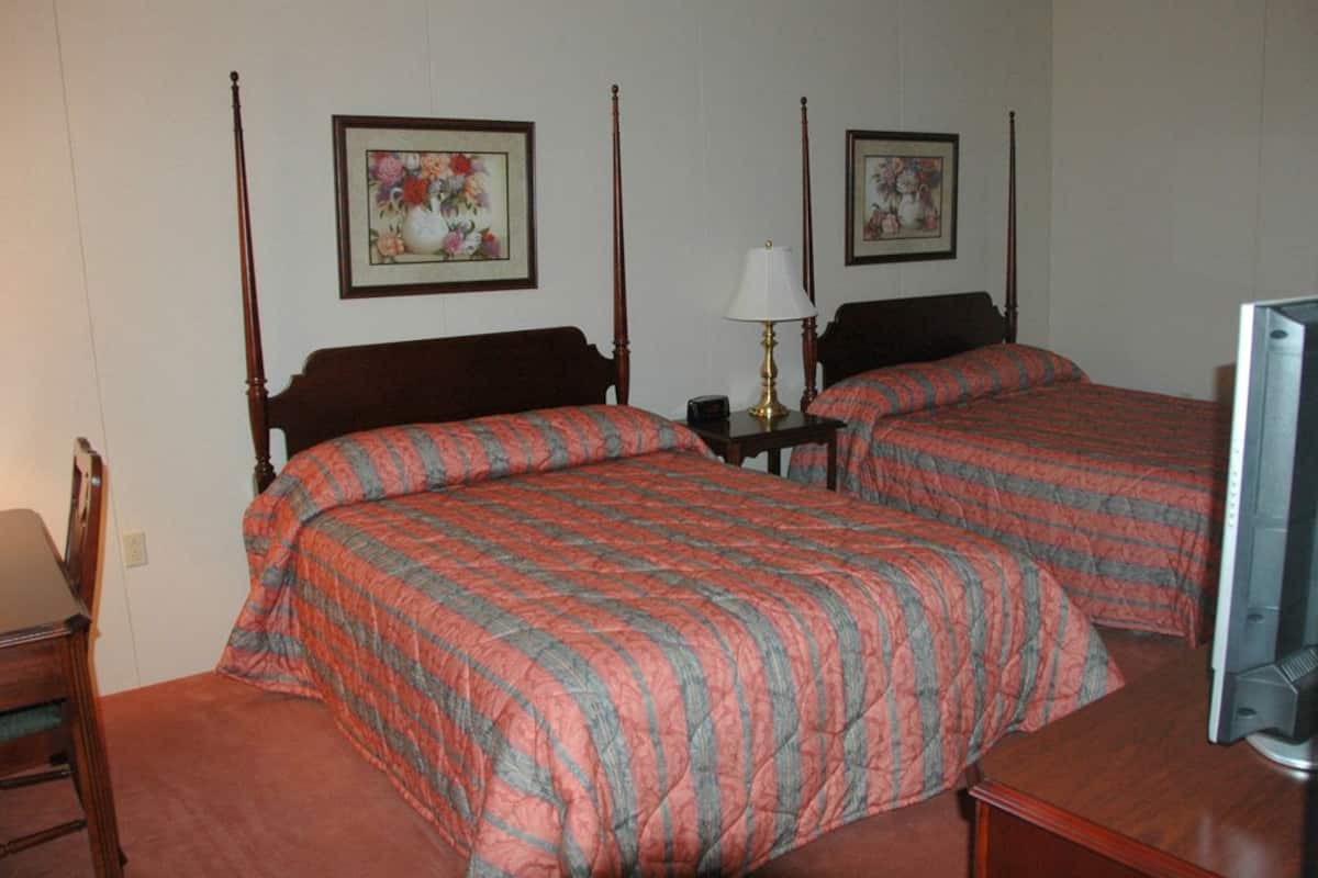 A room with two single beds, a desk, a chair, a lamp, and a television.