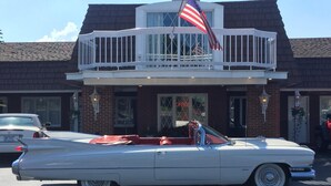 A classic white convertible car parked in front of a building with a balcony and an American flag.