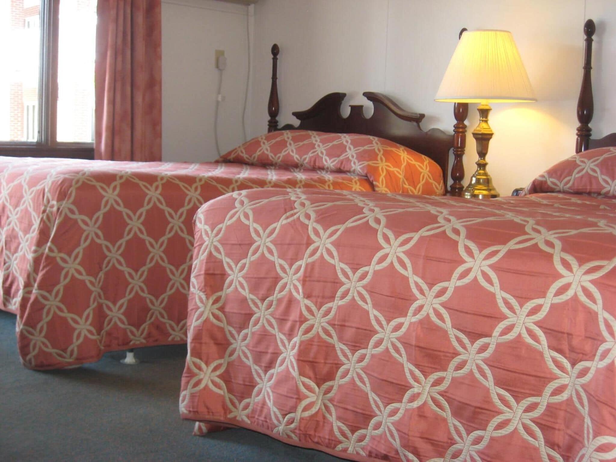 Habitación de hotel con dos camas, cada una con una colcha estampada, un cabecero de madera y una lámpara de noche.