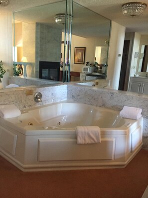 A large, white, freestanding bathtub in a bathroom with marble countertops, a large mirror, and a chandelier.