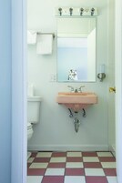 A bathroom with a white toilet, a pink sink, a mirror, and a checkered floor.