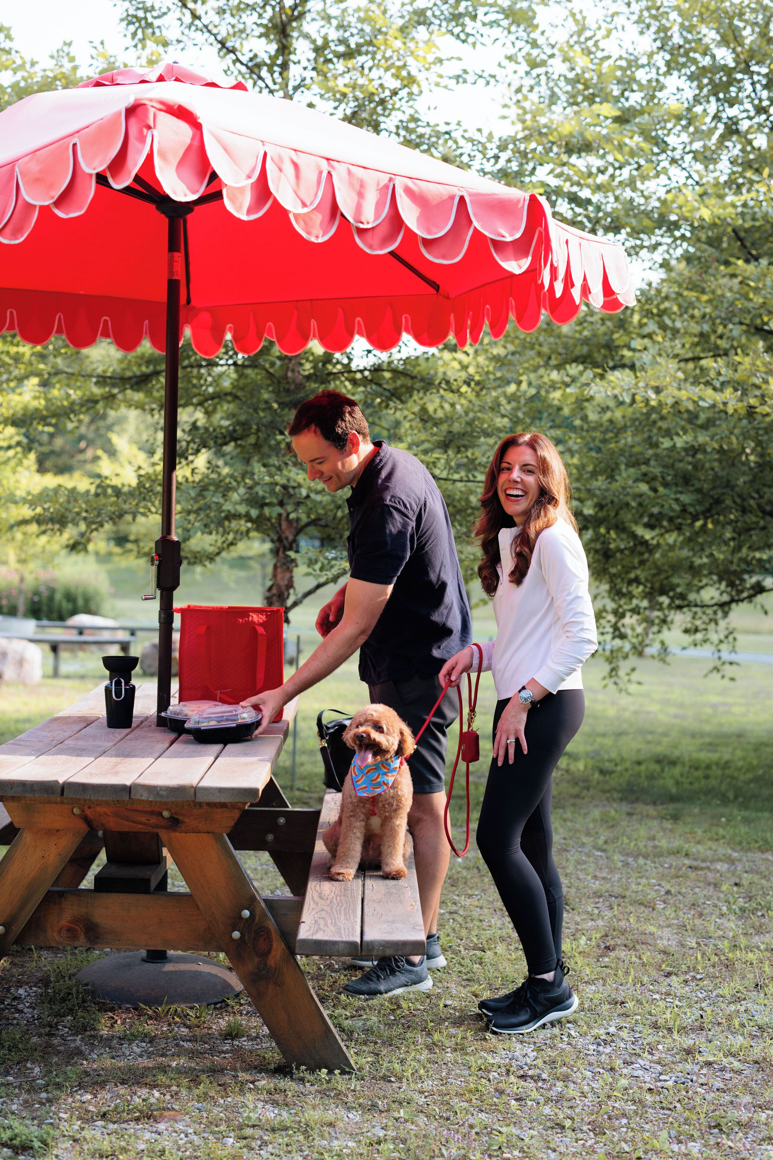 A picnic setup with a table, a red umbrella, and a dog.