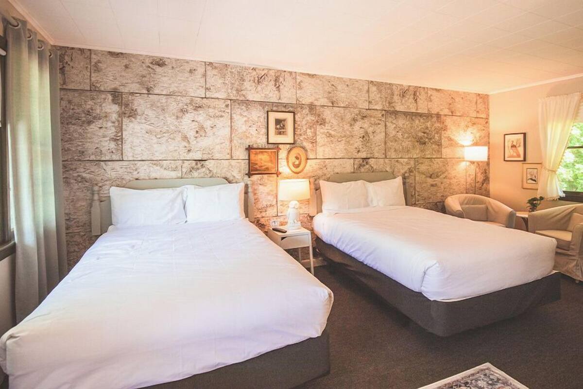A hotel room with two beds, a stone accent wall, a small desk, and a chair.