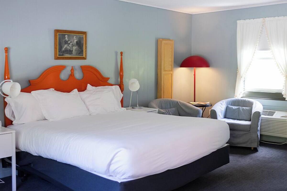 A hotel room with a large bed, a chair, a desk, and a lamp.